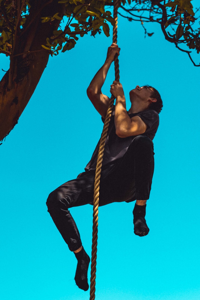 man in black tank top and black pants climbing on brown rope