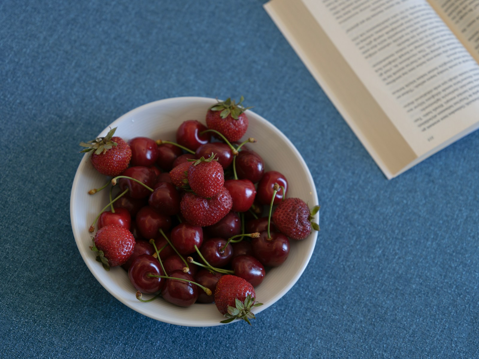 a bowl of cherries on a table next to a book